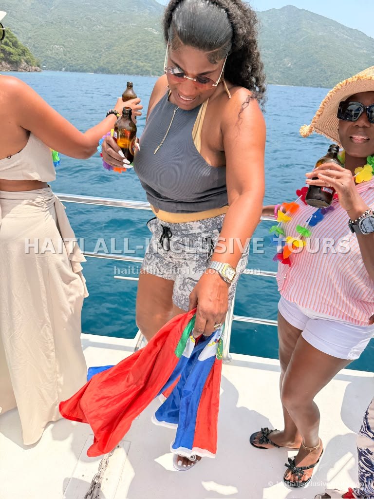 Guests toasting with drinks and the Haitian flag on the catamaran deck