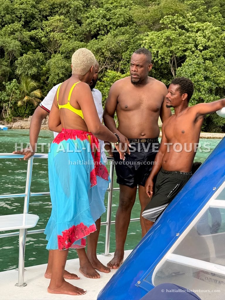 Guests and crew talking on the boat deck beside the green Haitian shoreline