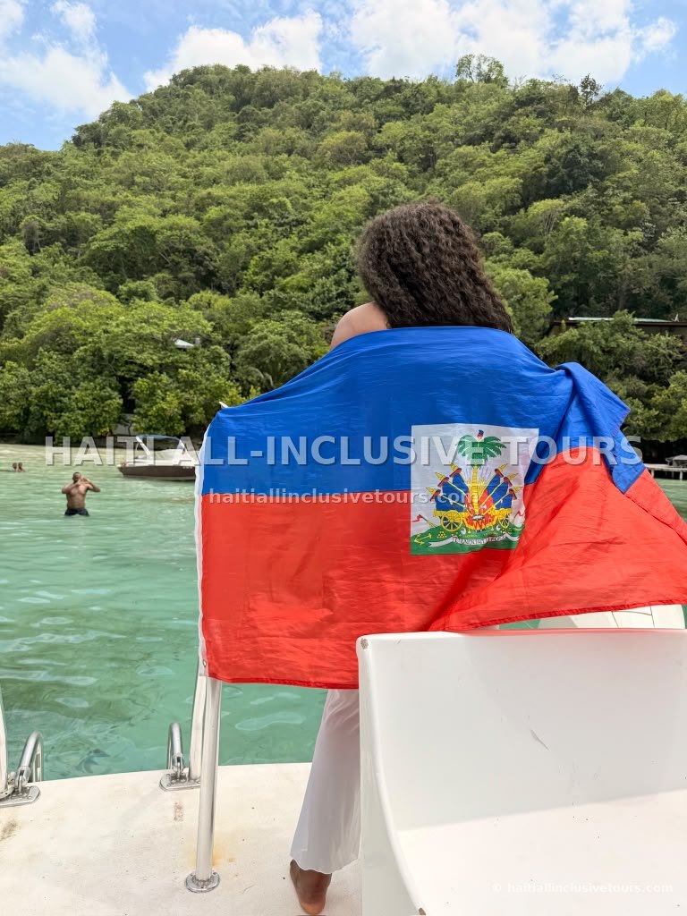 Guest draped in the Haitian flag facing the emerald cove and green hillside