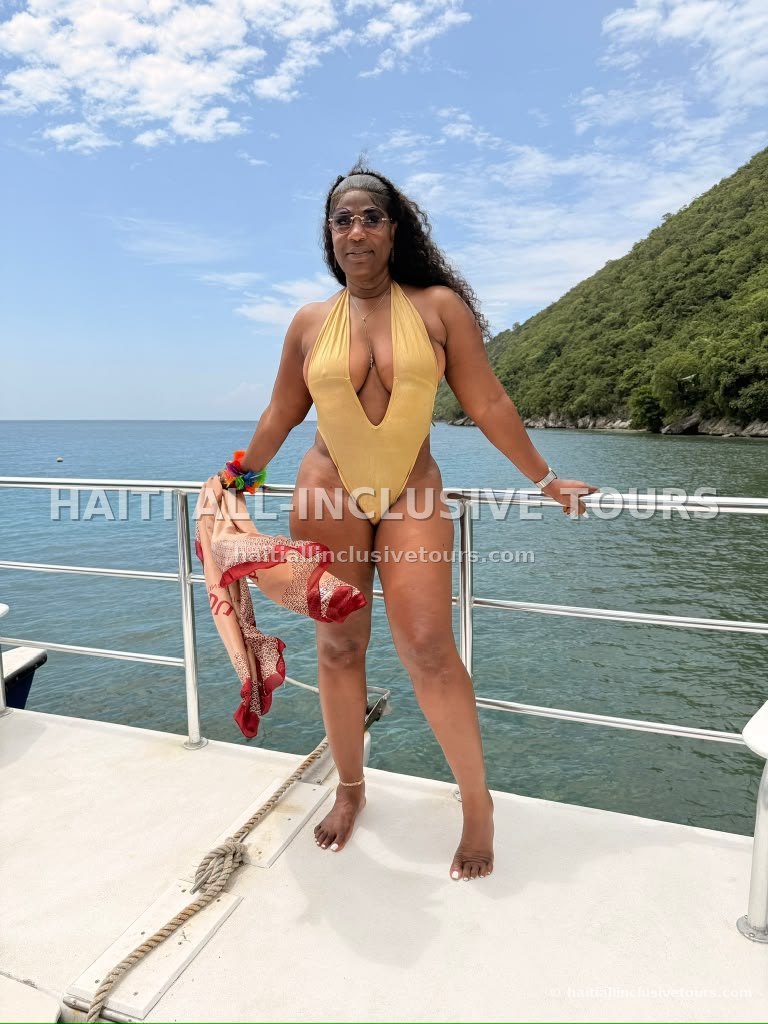 Guest posing on the catamaran deck along the green Northern Haiti coastline